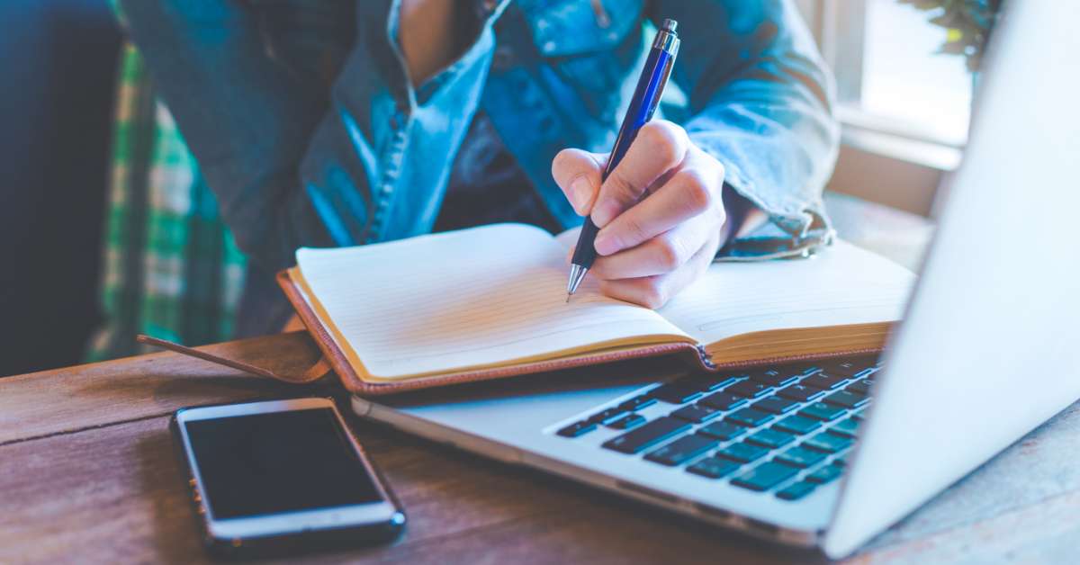 Someone writing in a notebook on top of a laptop | Struggling to Create Content That Converts? Try These Tips